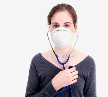 A white woman with dark hair holds a stethoscope to her own chest. She is wearing a paper mask and a gray shirt.