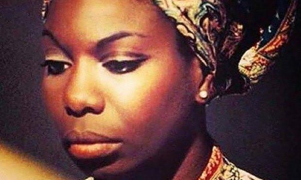 Image of the beautiful Nina Simone, in a matching head wrapper and dress her eyes looking downward and light reflecting off her dark brown skin. Credit "What Happened Ms. Simone?"