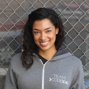 This is an image of Code 2040 CEO Laura Weidman POwers. She is a young woman with long black hair and brown skin. She is wearing a gray zip up hoodie and smiling brightly.