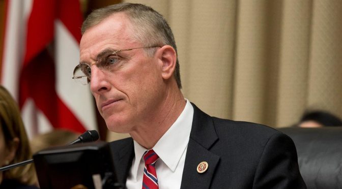This is an image of Congressman Tim Murphy from the shoulders-up. He is a white older man with thinning gray hair and glasses. He is wearing a red tie. There is a large American flag behind him.
