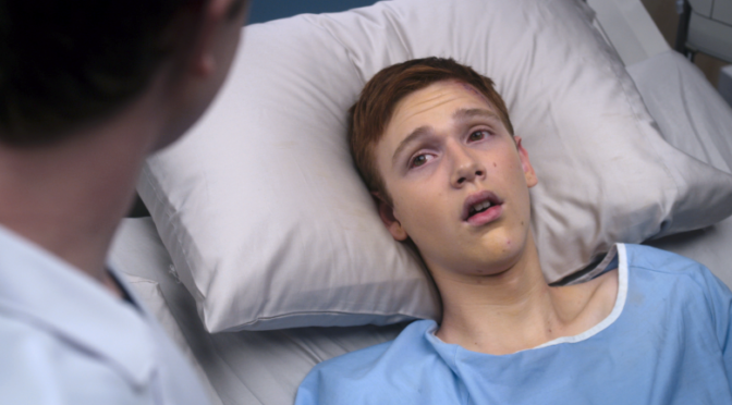This is an image of actor Coby Bird. He is a white teen boy with red hair. He is wearing a blue hospital gown and lying in a hospital bed.